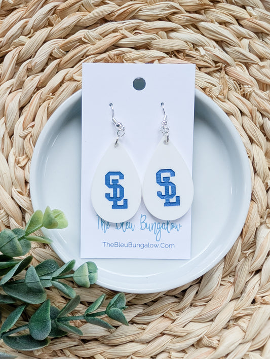Pair of earrings with 'S' design on a white card with brand name, placed on a woven surface with green leaves.